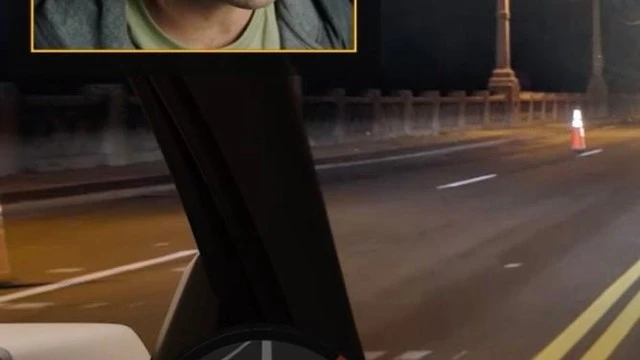An adult male seen from inside a car driving on a dark city street at night, illuminated by street lights.