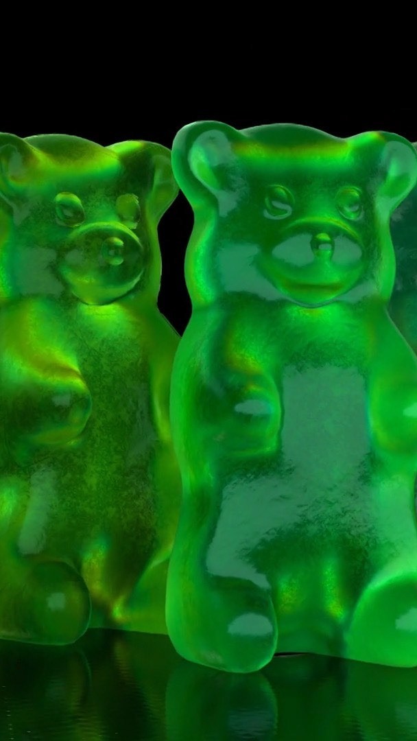 Close-up of green gummy bears on a reflective surface against a black background, showcasing their translucent texture.