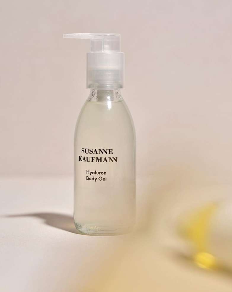 A clear bottle of Susanne Kaufmann Hyaluron Body Gel with a pump stands on a light surface with an off-white backdrop.