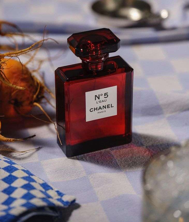 Close-up of Chanel No. 5 L'Eau perfume bottle with a red rectangular bottle and multifaceted stopper on a checkered tablecloth.