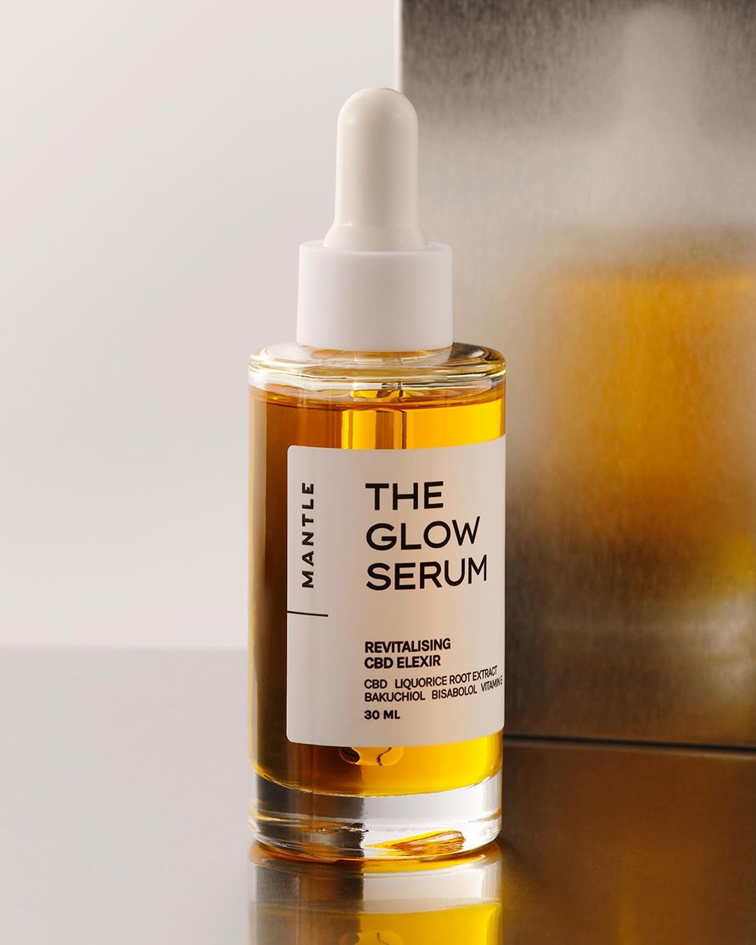 The Glow Serum by Mantle in a clear glass bottle with a white dropper, set against a gradient neutral background.