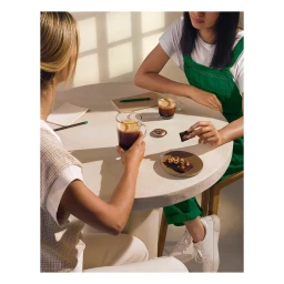 Two women seated around a round table with coffee mugs and chocolate pieces by photographer Alice Cuvelier