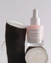 Pink serum bottle resting on sliced dark roots against a plain light background