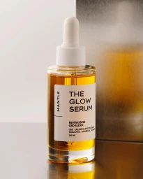 Glass dropper bottle of skincare serum with amber liquid and white cap on a reflective surface against a metallic background