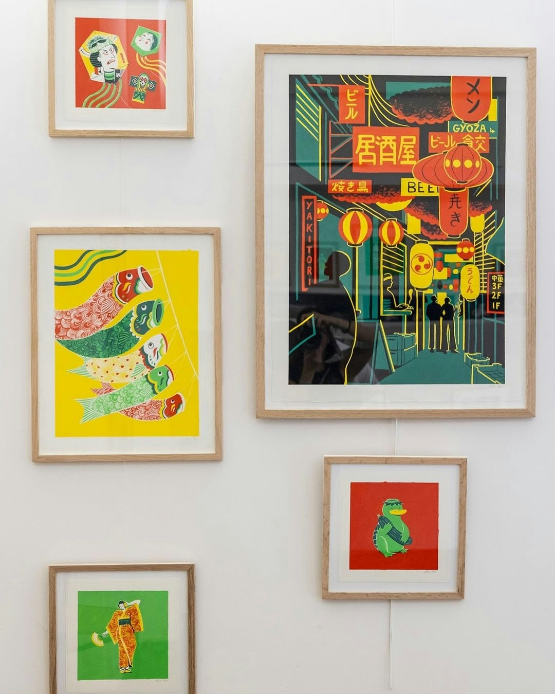 Framed illustration art prints on a white wall, featuring various designs including Japanese street scenes and cartoon characters.