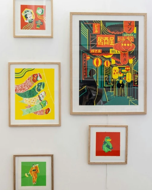 Framed illustration art prints on a white wall, featuring various designs including Japanese street scenes and cartoon characters.