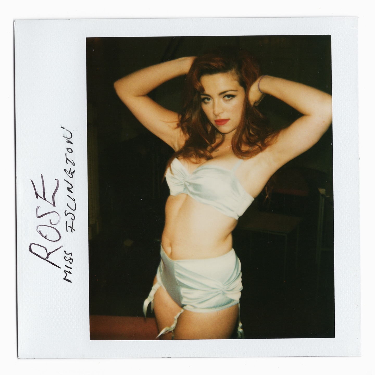 Glamorous woman poses indoors in lingerie. The photo is an artistic snapshot with hand-written text on the polaroid frame.