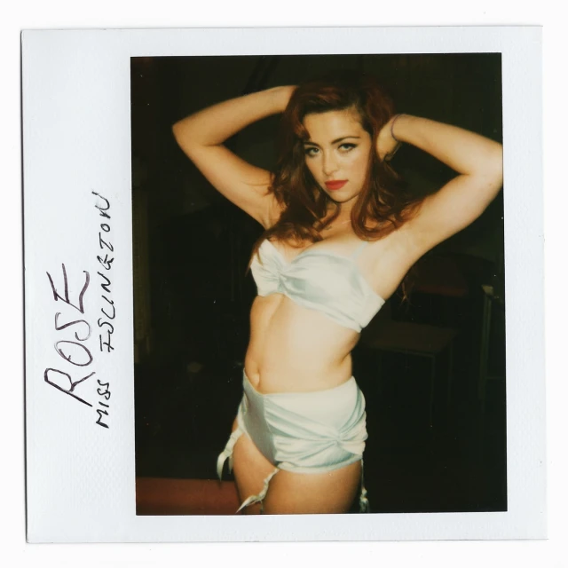 Glamorous woman poses indoors in lingerie. The photo is an artistic snapshot with hand-written text on the polaroid frame.