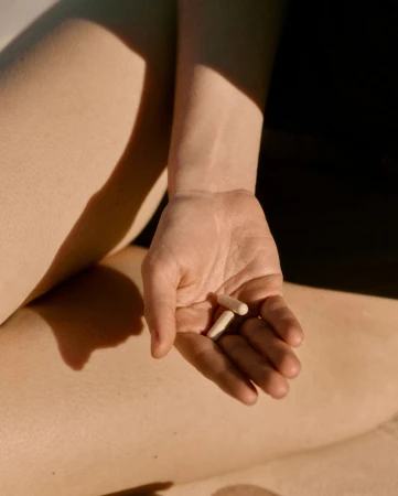 Close-up shot of a fair-skinned person holding two white capsules in their hand with a warm, light-filled background and shadows.