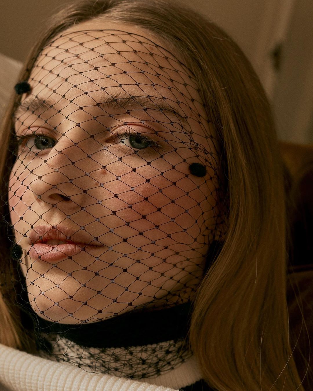 Close-up portrait of a young adult woman wearing a black dotted net veil, showcasing a beauty and fashion aesthetic.