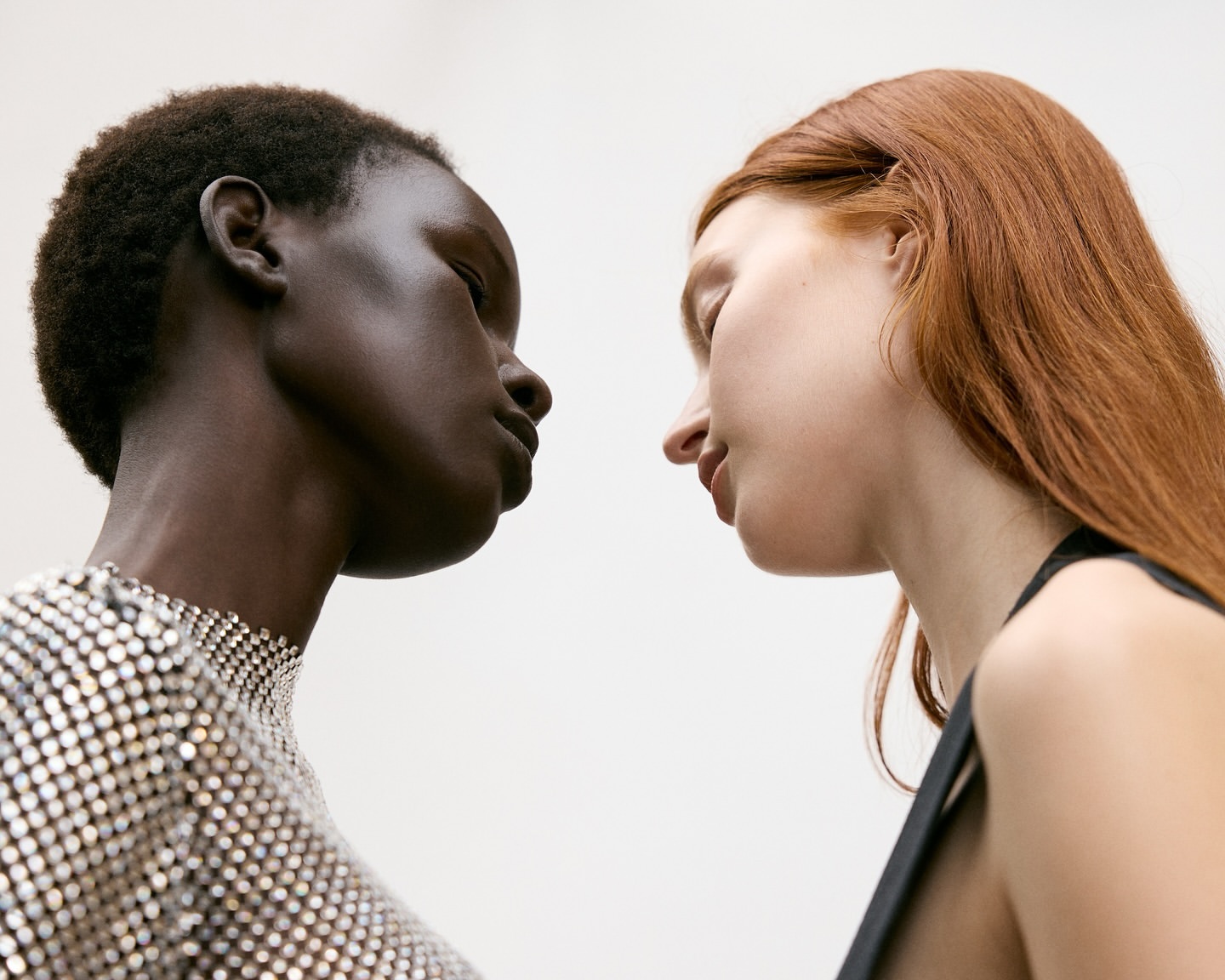 Two diverse women facing each other in a close-up portrait. The woman on the left has dark skin, while the one on the right has fair skin.
