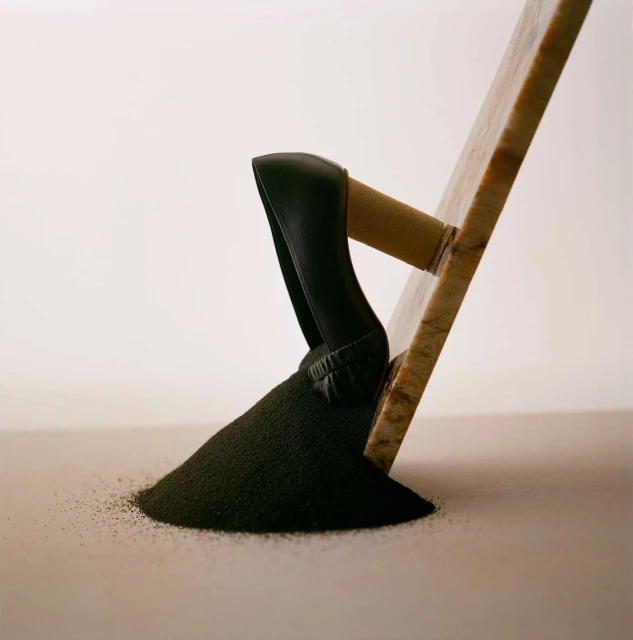 A construction trowel rests on a pile of black granular material against a pale background, showcasing texture and form.