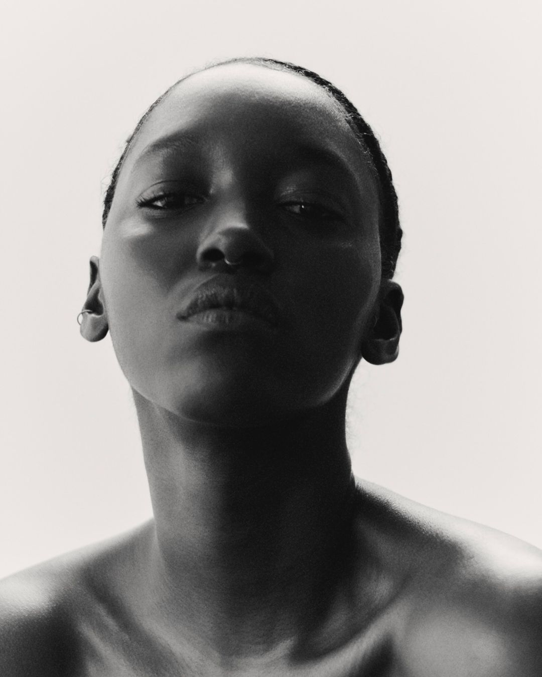 Striking black and white portrait of an African American woman with a bare upper body against a bright, neutral backdrop, eye-level.