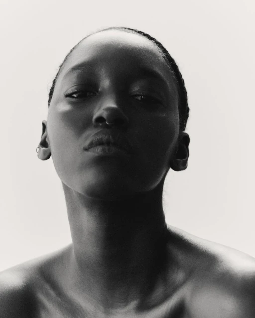 Striking black and white portrait of an African American woman with a bare upper body against a bright, neutral backdrop, eye-level.