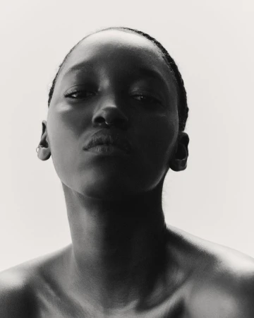 Striking black and white portrait of an African American woman with a bare upper body against a bright, neutral backdrop, eye-level.