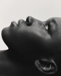 Profile portrait of a black woman in profile shot from below against a plain light background by Alice Jacquemin in Paris.
