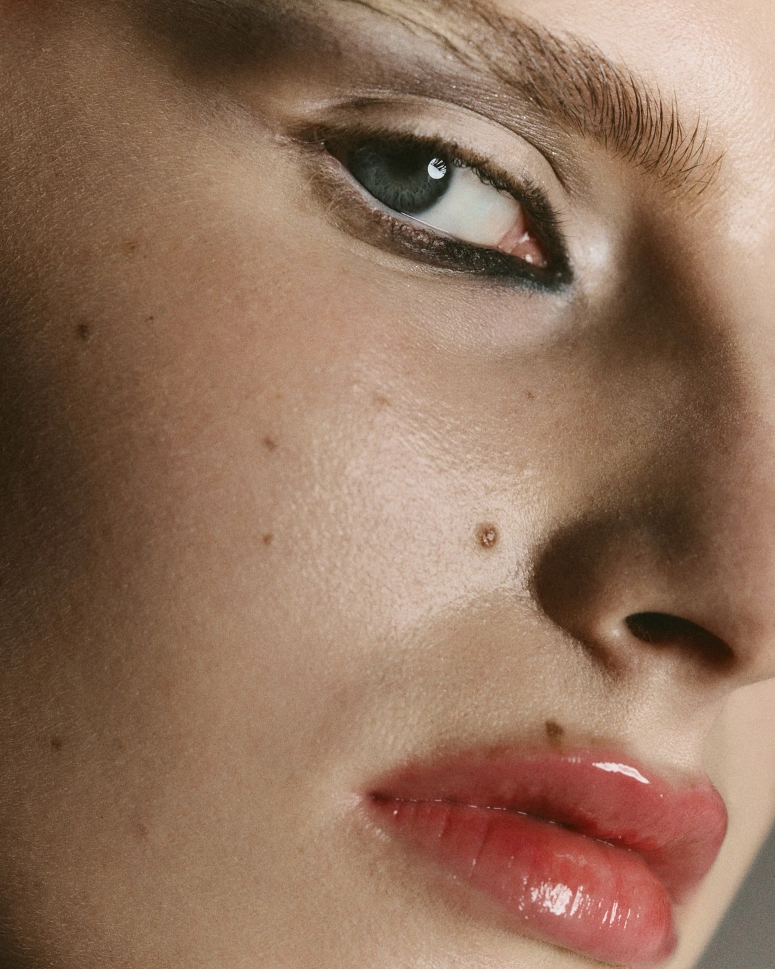 Close-up beauty portrait of a woman face with dark eyeliner and glossy lips photographed by Alice Jacquemin