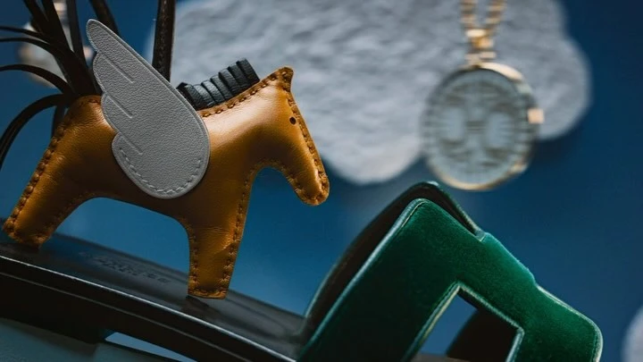 Close-up of a brown leather horse-shaped charm with white wings on a green platform, against a blurry blue background.