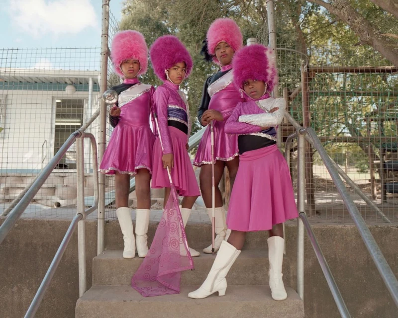 Four children in pink band uniforms stand on stairs in an outdoor setting, two holding batons, showcasing a unique group performance.