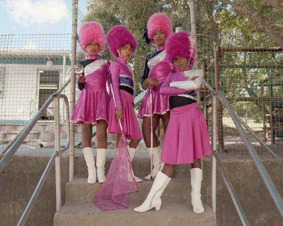 Four children in pink band uniforms stand on stairs in an outdoor setting, two holding batons, showcasing a unique group performance.