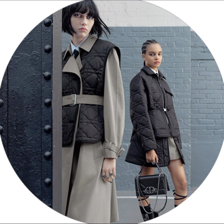 Two women pose in stylish quilted outerwear on a city street. One wears a vest over a trench coat; the other has a quilted jacket.