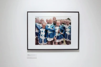 A framed photograph of a group of young female dancers wearing matching blue and white costumes displayed on a white wall.