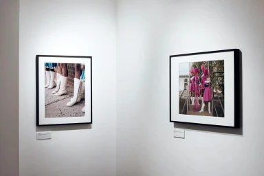Two framed photographs displayed on a plain white gallery wall showcasing subjects in boots and uniforms.