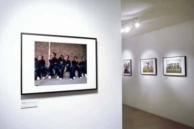 Framed photographic prints displayed in a white art gallery with track lighting, featuring a group portrait of children