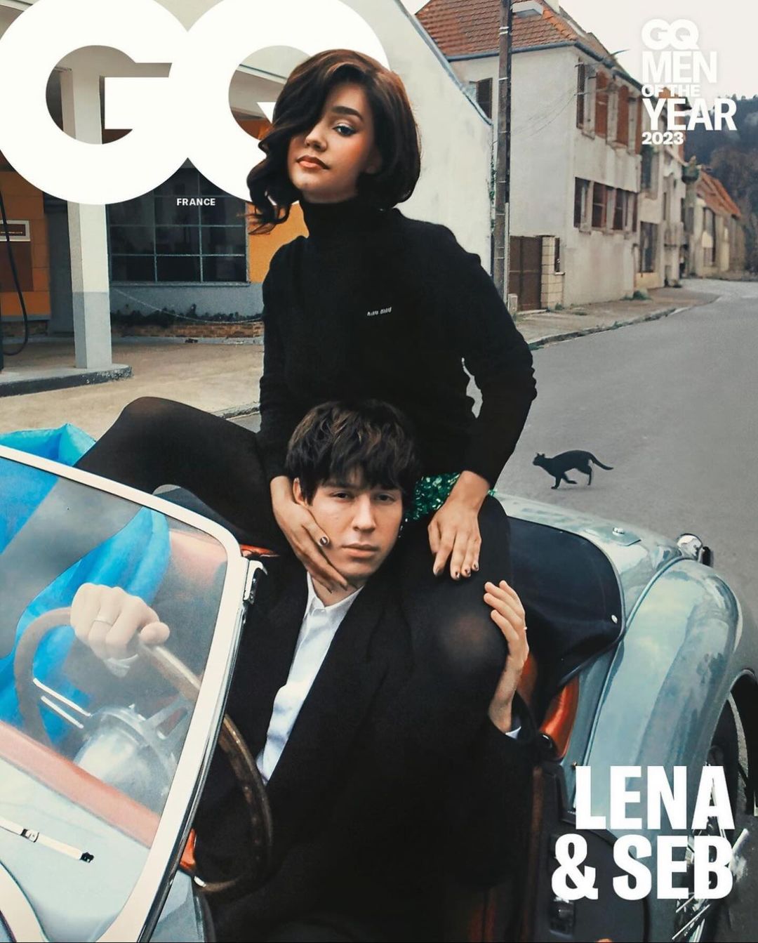 GQ magazine cover featuring a woman in a black turtleneck sitting on a man's shoulders, with a vintage car and European street as backdrop.