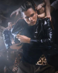 Man wearing a glossy black jacket surrounded by reaching hands in a portrait by photographer Alice Moitie