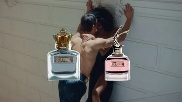 Two Scandal fragrances are positioned in front of a couple embracing against a brick wall, capturing a moment of intimacy.