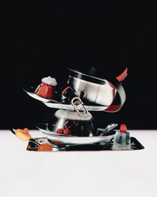 Elevated still life photography of a food arrangement with small desserts, cherries, and silver serving dishes against black and white backgrounds.