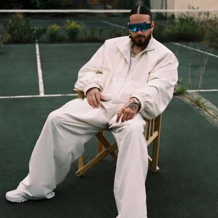 Man with beard and sunglasses seated in a chair on a tennis court wearing a white tracksuit by photographer Alice Rosati