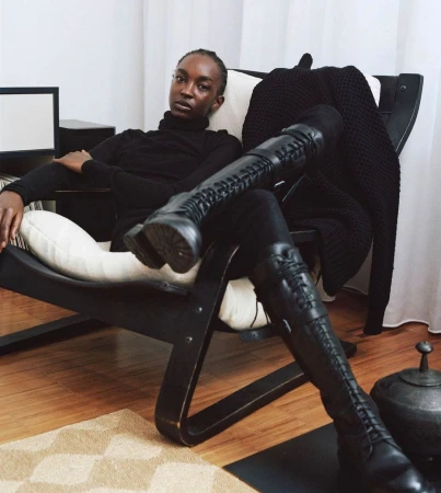 Black woman seated in a black armchair wearing a black turtleneck and tall black lace-up boots, photographed by Alice Rosati