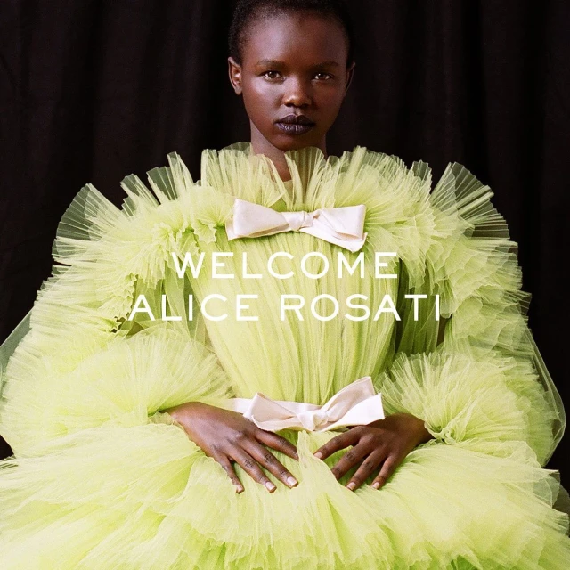 Elegant Black woman in a light green ruffled gown with large bows, against a dark backdrop, creating a striking and fashionable portrait.