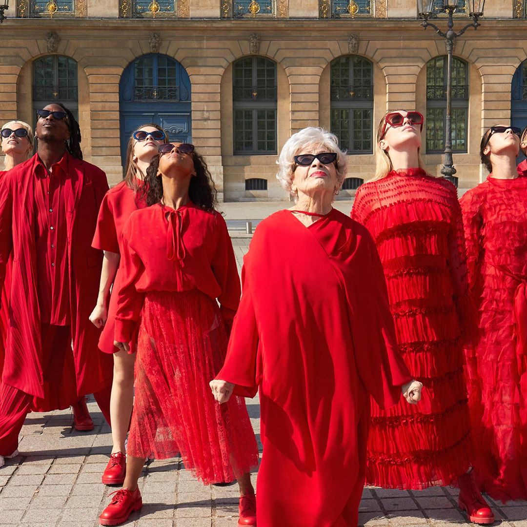 Group of diverse women and men standing together outside in Paris, France, wearing red clothing and sunglasses, looking up towards sky.