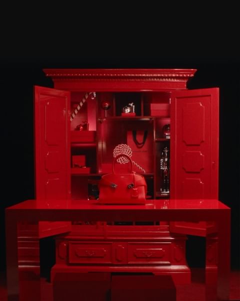 Elegant red handbag on a matching red dresser with open cabinet, studio lighting, and a dark background creating a luxurious feel.