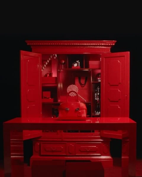 Elegant red handbag on a matching red dresser with open cabinet, studio lighting, and a dark background creating a luxurious feel.