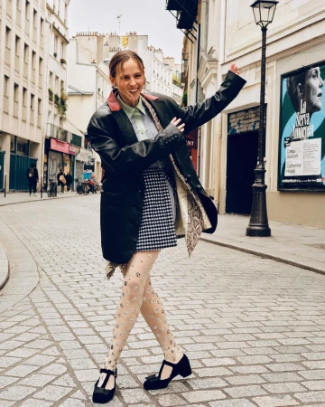 Smiling woman in a black leather jacket and patterned skirt dancing on a cobblestone Paris street by photographer Alice Rosati
