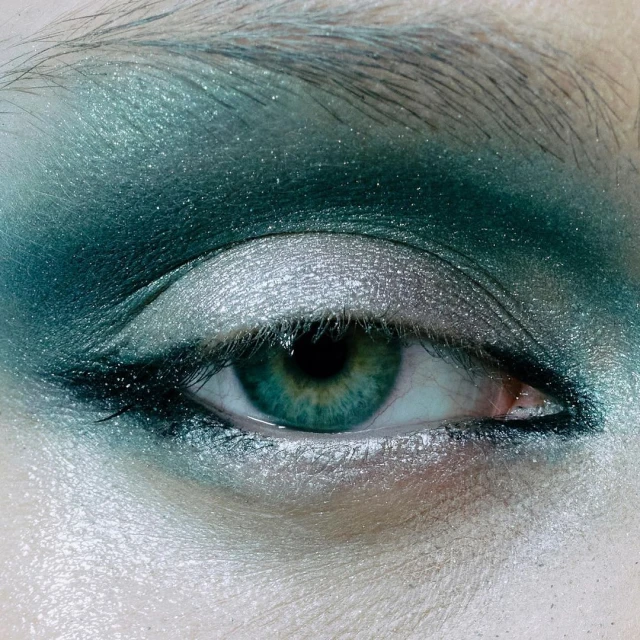 Close-up of a woman's eye featuring vivid green irises and expertly applied emerald and silver eyeshadow for a striking beauty look.