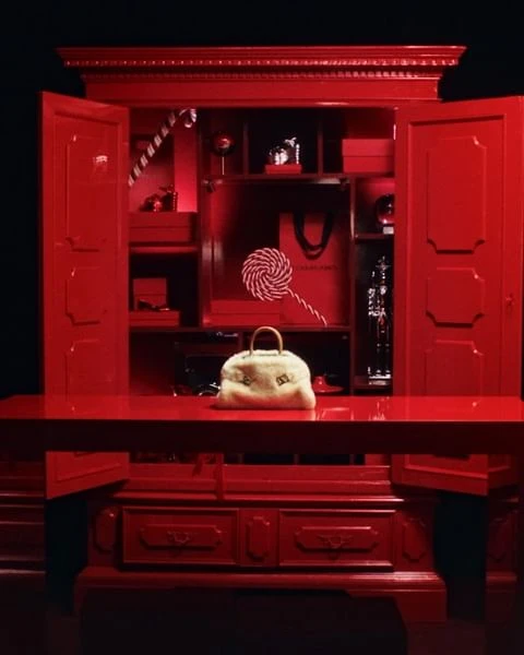 Red armoire with gifts and a fur purse, sitting on a table in front of a dark background, high-fashion styling.