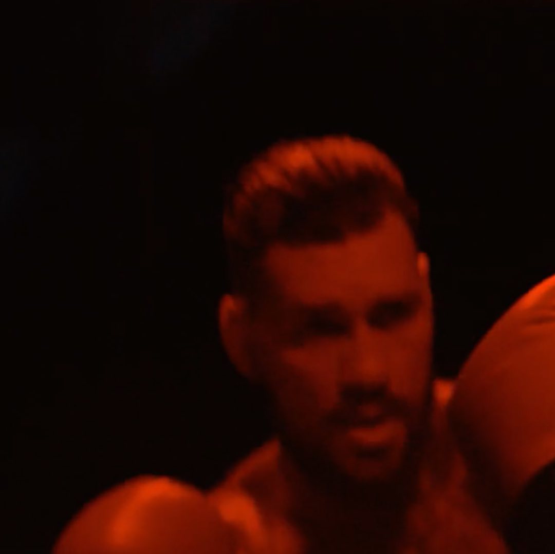 Man with boxing gloves in a dimly lit, dark boxing gym. The scene features a red color cast and a close-up portrait.