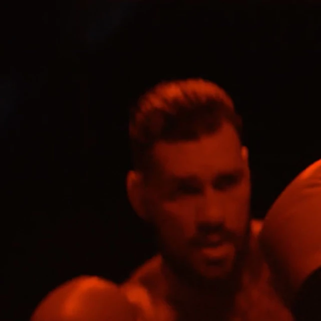 Man with boxing gloves in a dimly lit, dark boxing gym. The scene features a red color cast and a close-up portrait.