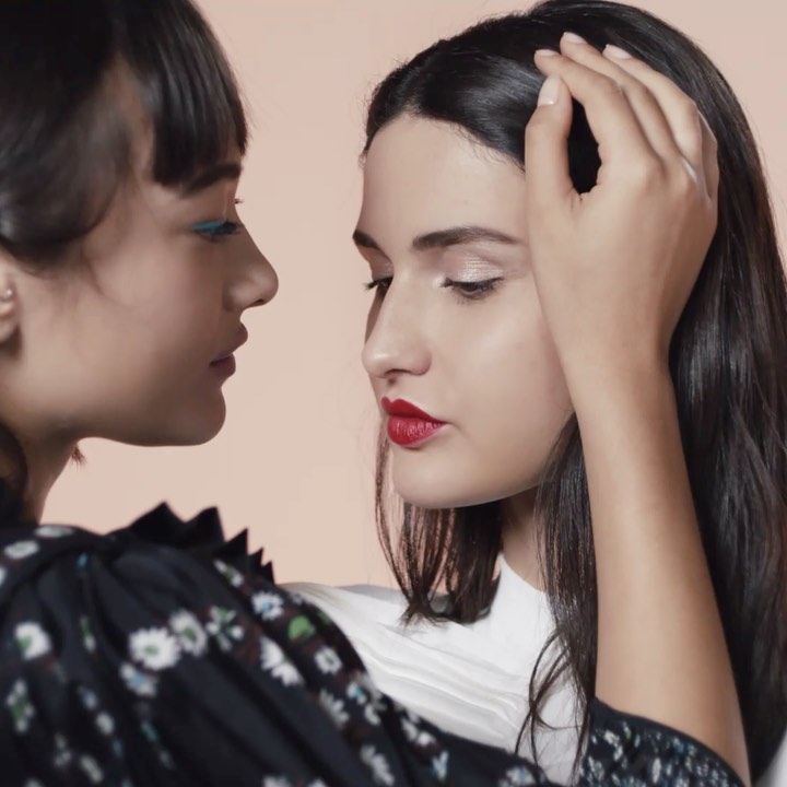 Two women posing closely with one hand gently touching her hair, captured in soft studio lighting against a neutral backdrop by Alice Rosati.