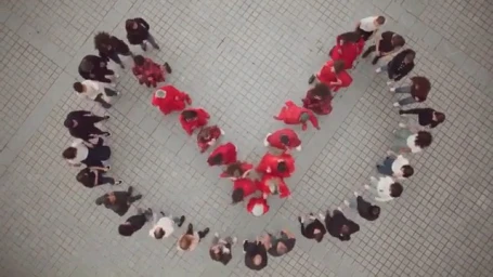 High-angle aerial view of a large group of people arranged in a heart shape on a paved square by photographer Alice Rosati