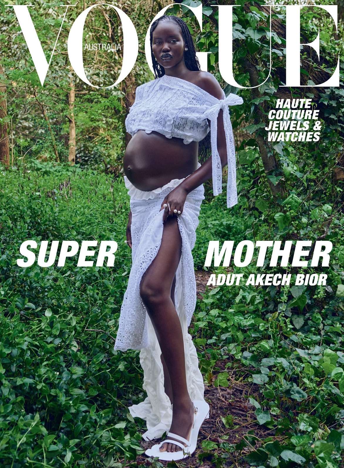 Vogue Australia cover featuring a pregnant Black woman, Adut Akech Bior, in a white lace dress, posing outdoors in a lush, green forest setting.