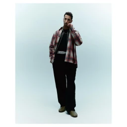 Man wearing plaid shirt and dark trousers standing against a pale grey seamless studio backdrop
