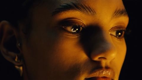 Close-up portrait of an adult female with brown eyes, warm lighting, and dark background. The focus is on the model's face.