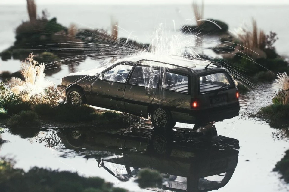 Antique station wagon vehicle is partially submerged in water as it's being struck by sparks in an outdoor setting with greenery.