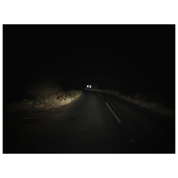 Dark asphalt road with white line markings curving ahead under bright vehicle headlights at night in rural environment.